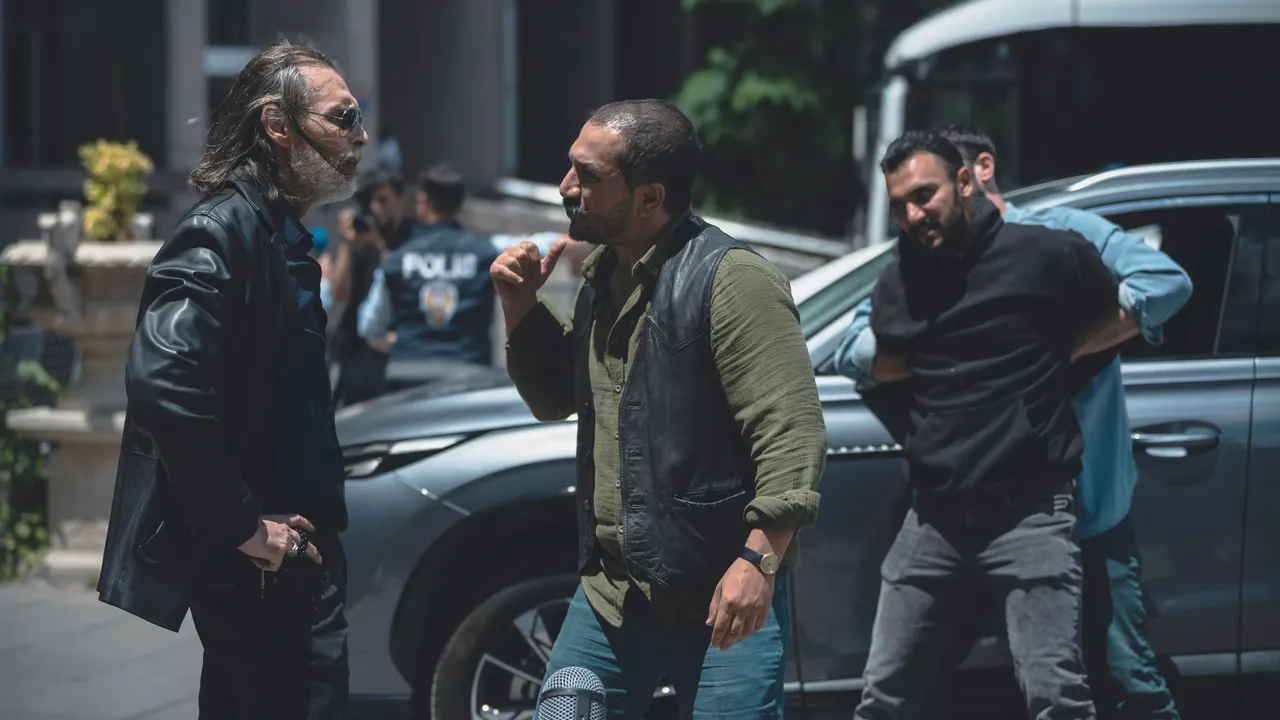 Üç adam park edilmiş bir otomobilin yanında konuşuyor.