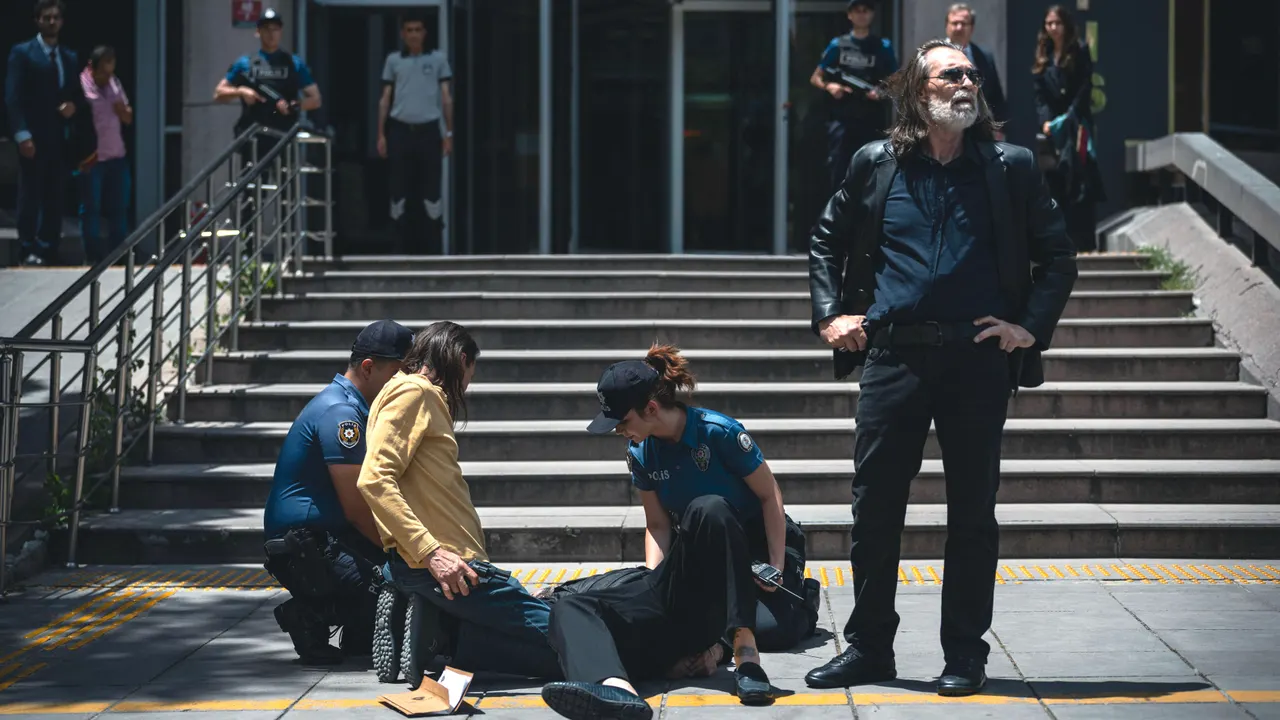 Behzat merdivenlerin önünde dururken arkasındaki ekip yerdeki bir kişiyle ilgileniyor.